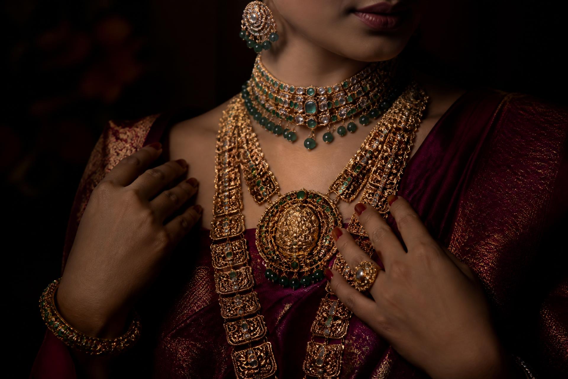 Layered heritage gold and emerald jewellery worn with burgundy silk